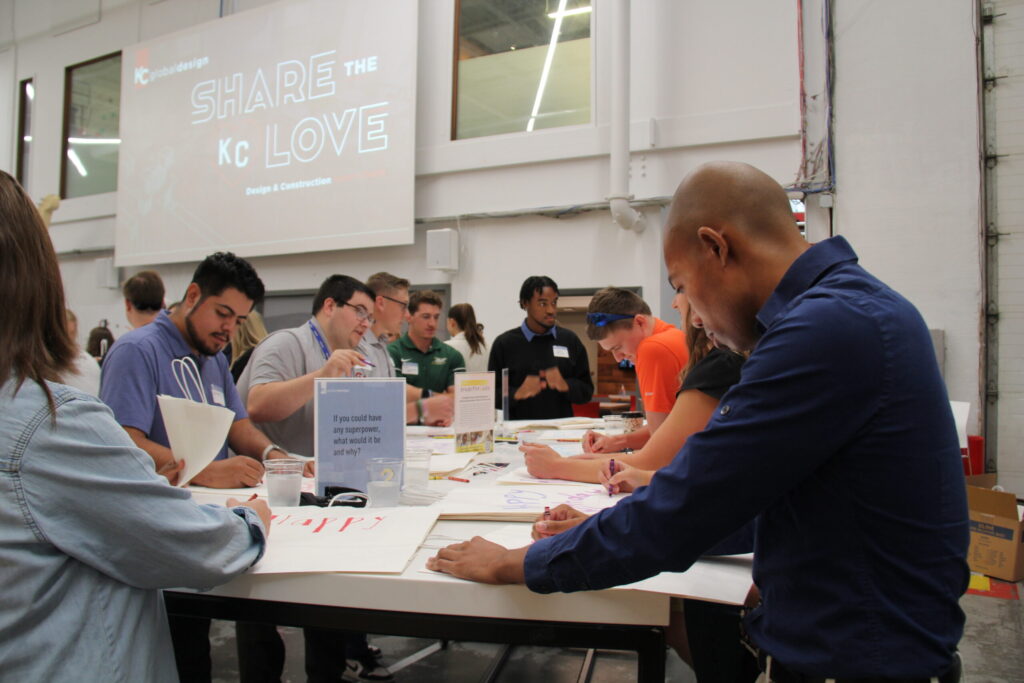 Young professionals working at tables, with a screen in the background reading Share the KC Love