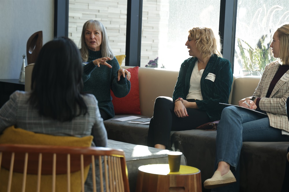A woman gestures to others sitting around a coffee table.