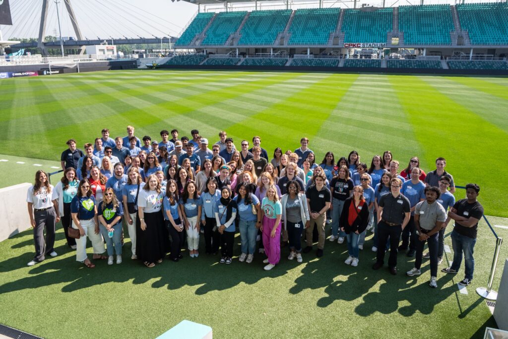 A large group poses for a group photo on a soccer field in the CPKC Stadium.