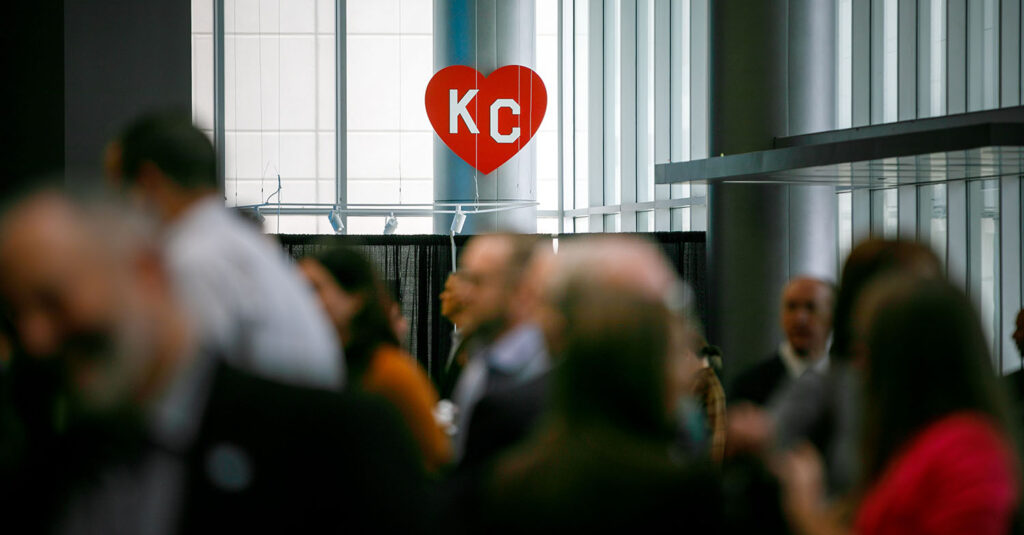 Red KC heart cardboard cutout, with a crowd of people blurry in the foreground