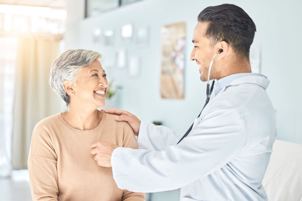 Male doctor checking an elderly female with a stethoscope, both smiling