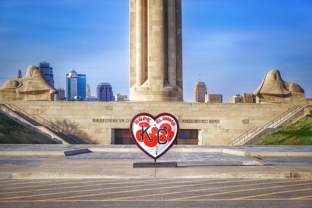 A KC heart sculpture painted with red poppies sitting in front of Liberty Memorial, a large stone memorial