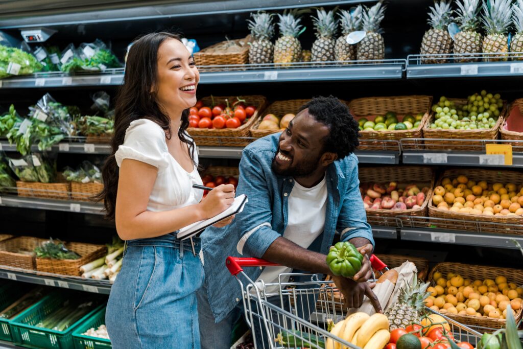 Young couple at the grocery store, woman holding a list and the man holding a green pepper, both smiling