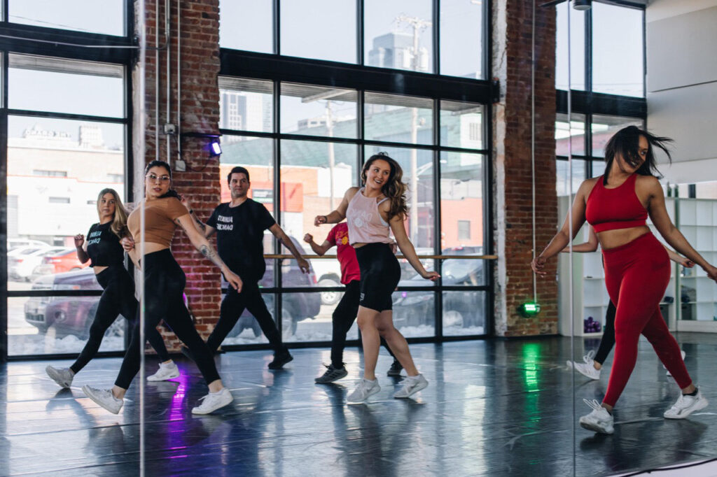 Young men and women in fitness clothes moving in an open studio room with glass walls