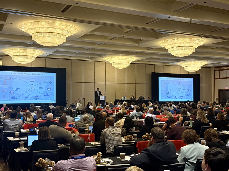 Man speaking in front of a large group of peopled seated at tables