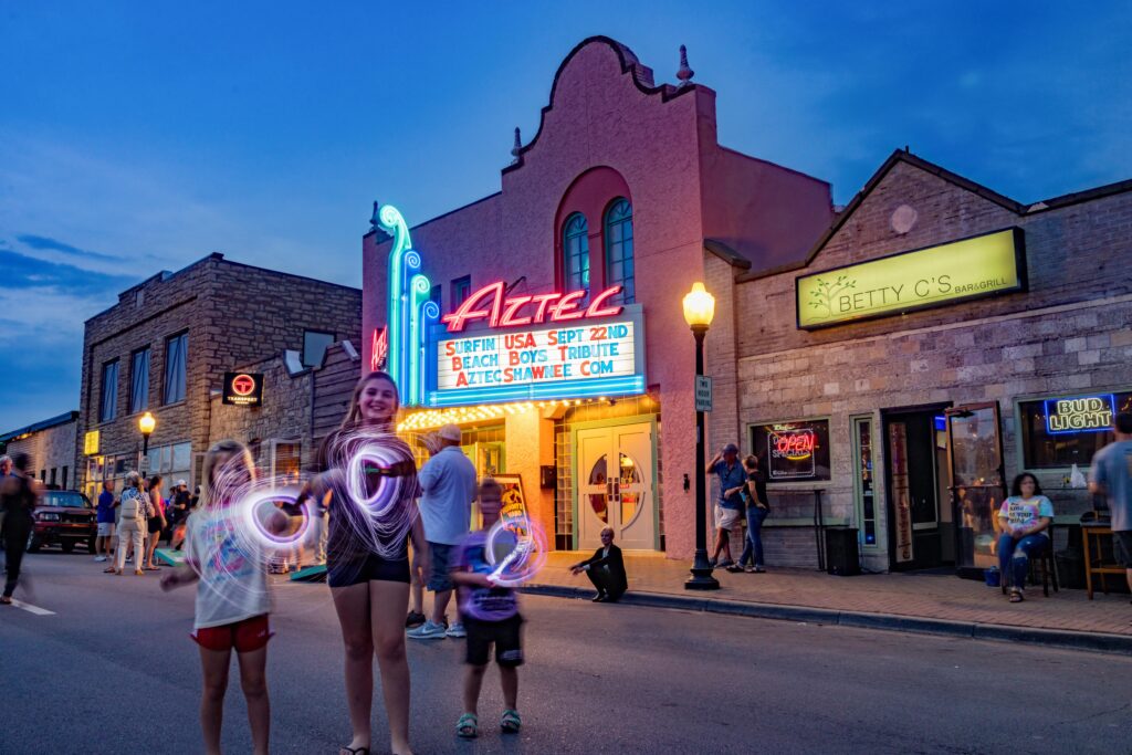 Kids playing with glowsticks in early evening in front of a historic movie theater