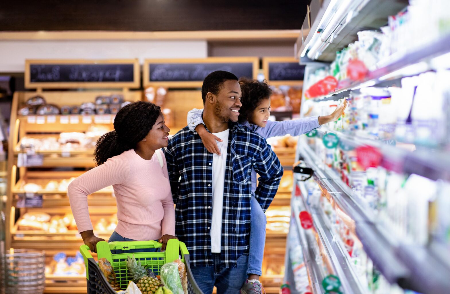 A couple and their child pushing a cart and browsing groceries.
