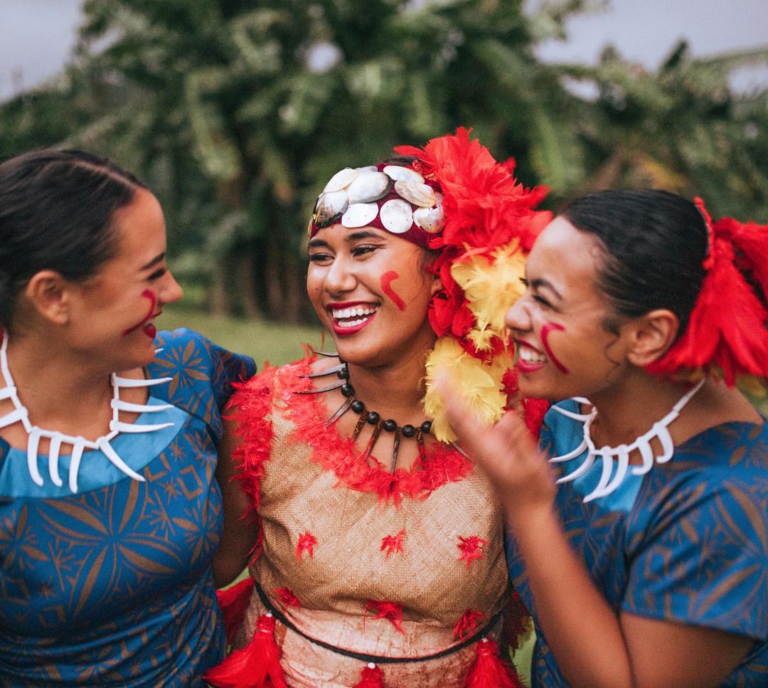 Three people in Polynesian dress laugh together.