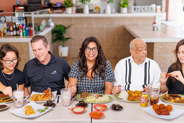Woman smiling, sitting at a table of food with her adult family members
