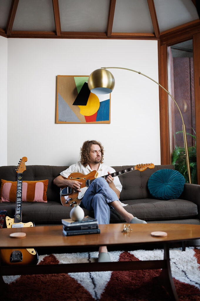 Kevin Morby sitting on a couch and playing guitar. 