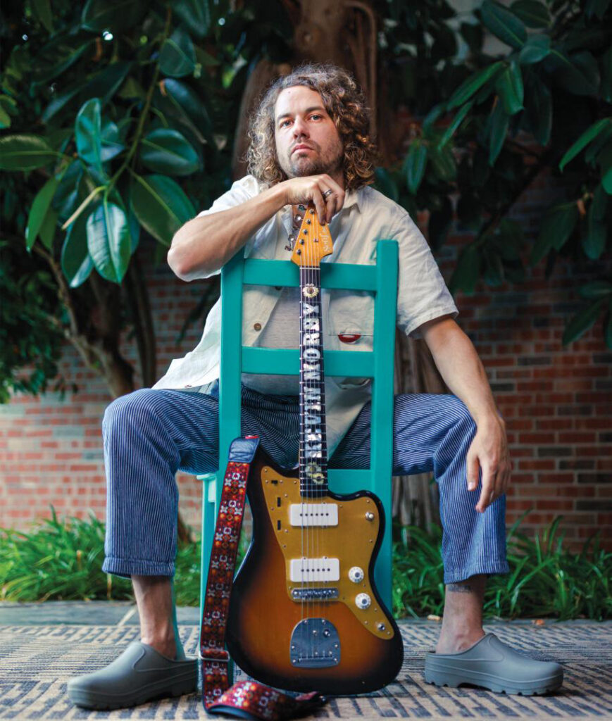 Kevin Morby sitting down and holding his guitar. 