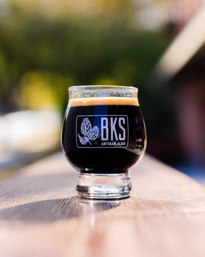 Short tulip beer glass filled with a dark beer, with BKS engraved on the side