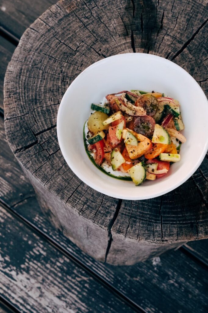 White bowl of brightly colored chopped veggies, sitting on a wooden post