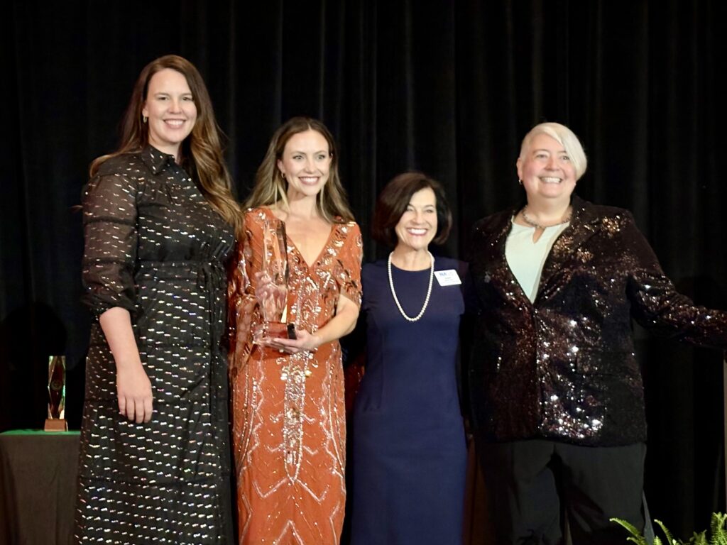 Four women smile with an award 