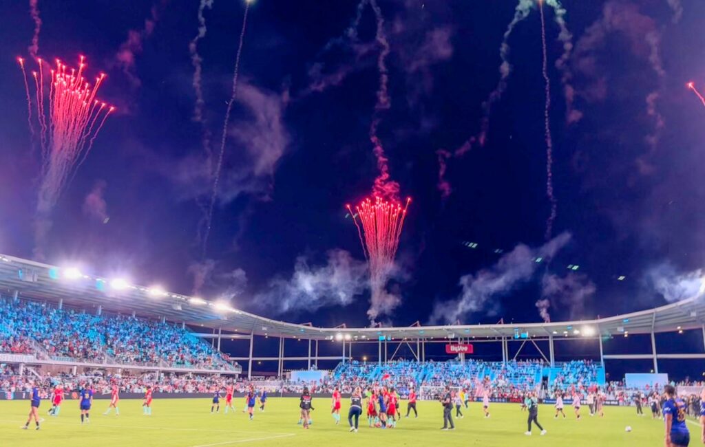 KC Current women's soccer team playing a pitch with fans in the stands and fireworks lighting up the sky