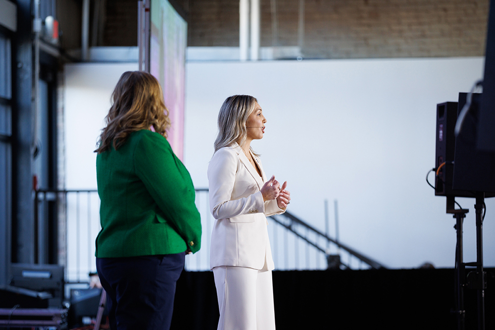 Danielle Hilton in a white suite and Alicia Bacon in a green jacket, standing on stage together