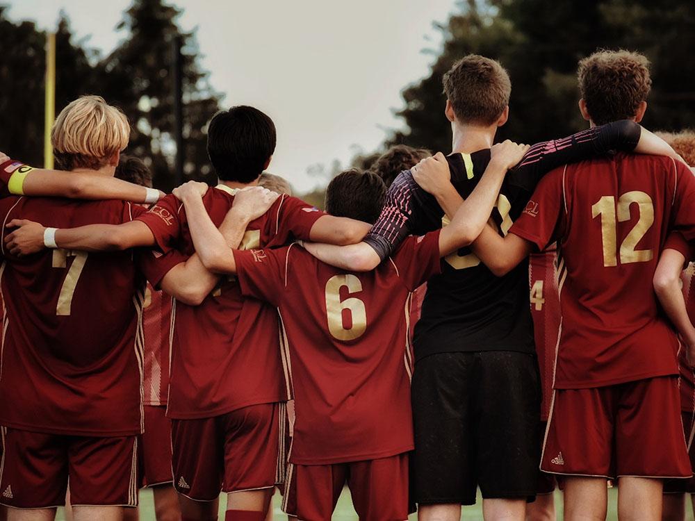 A group of children soccer players, seen from the back, with their arms around each other's shoulders