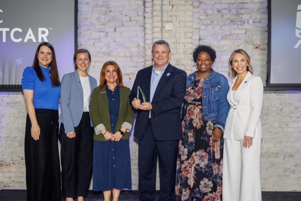 KC Streetcar Authority team standing on stage with Danielle Hilton and Erin Roebuck, holding a green glass award