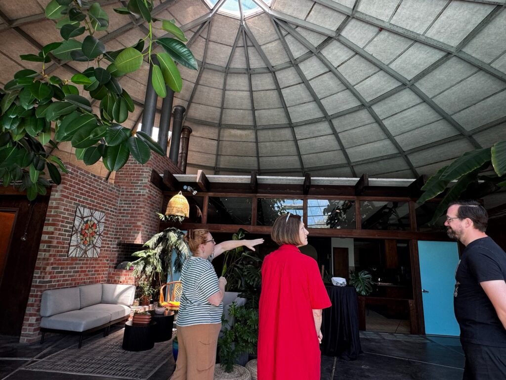 Three guests walking and talking in a large room with plants, brick walls and a large domed ceiling