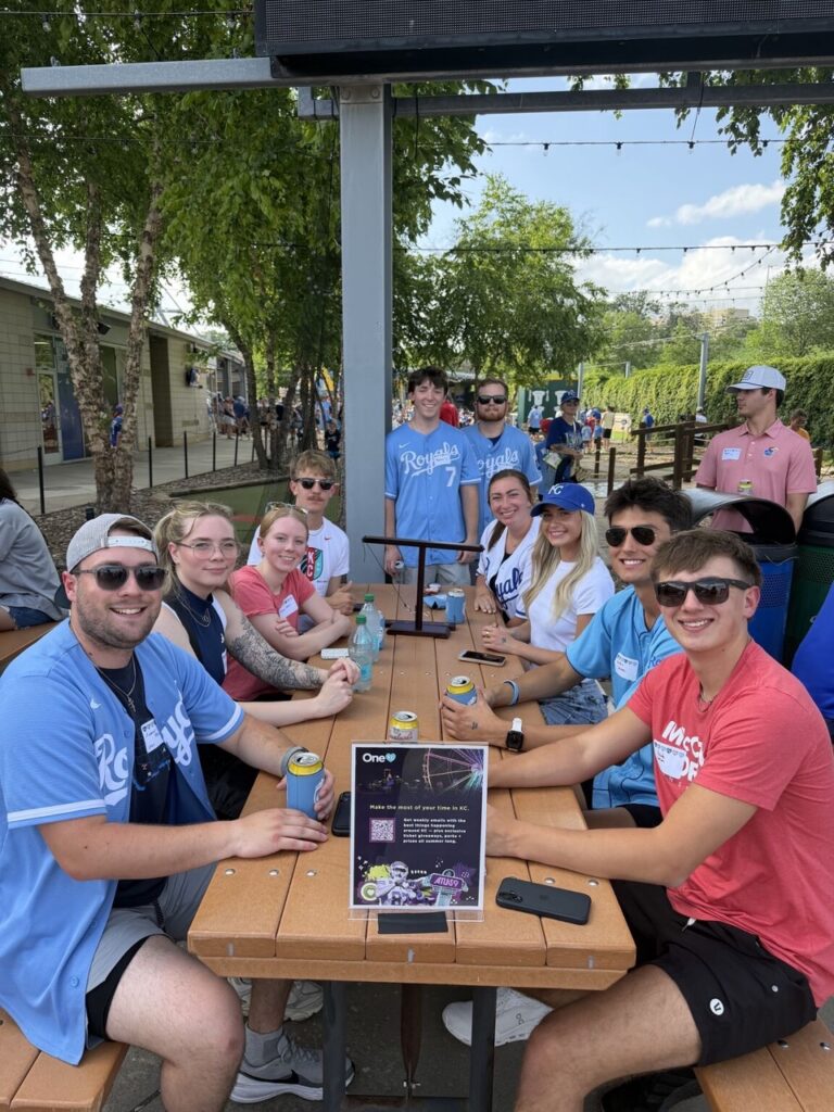 Group of interns dressed in Royals gear seated at a picnic table